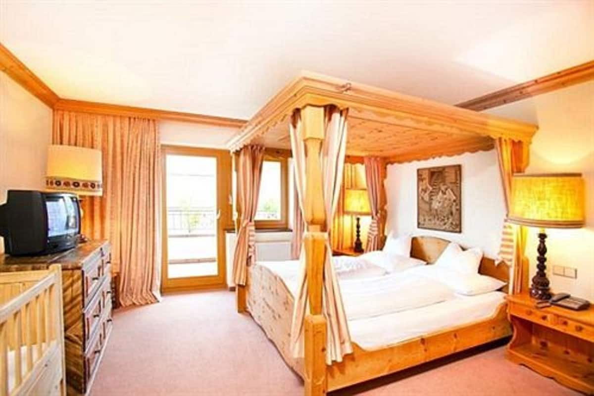 Un lit à baldaquin, un téléviseur posé sur une commode en bois et un tableau accroché au mur.