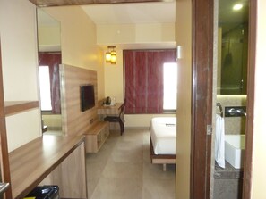 A hotel room with a wooden desk, a bed, a TV, and a bathroom visible through a glass door. - Hotel New Bengal (Mumbai)