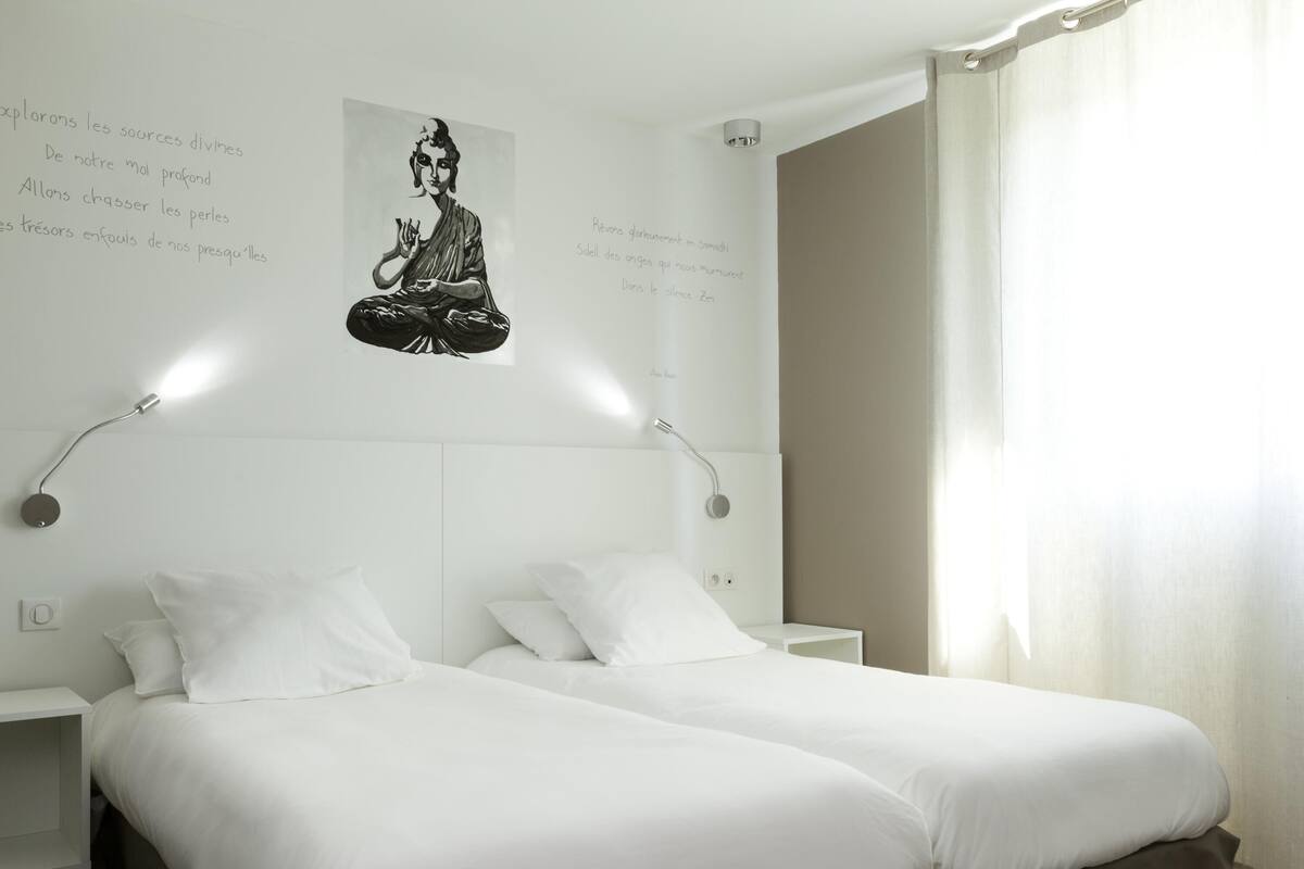 Una habitación de hotel con dos camas, una lámpara fijada a la pared y un cartel con la imagen de una persona meditando.