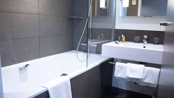 A modern bathroom with a glass-enclosed shower, a white bathtub, and a sink with a mirror above it.