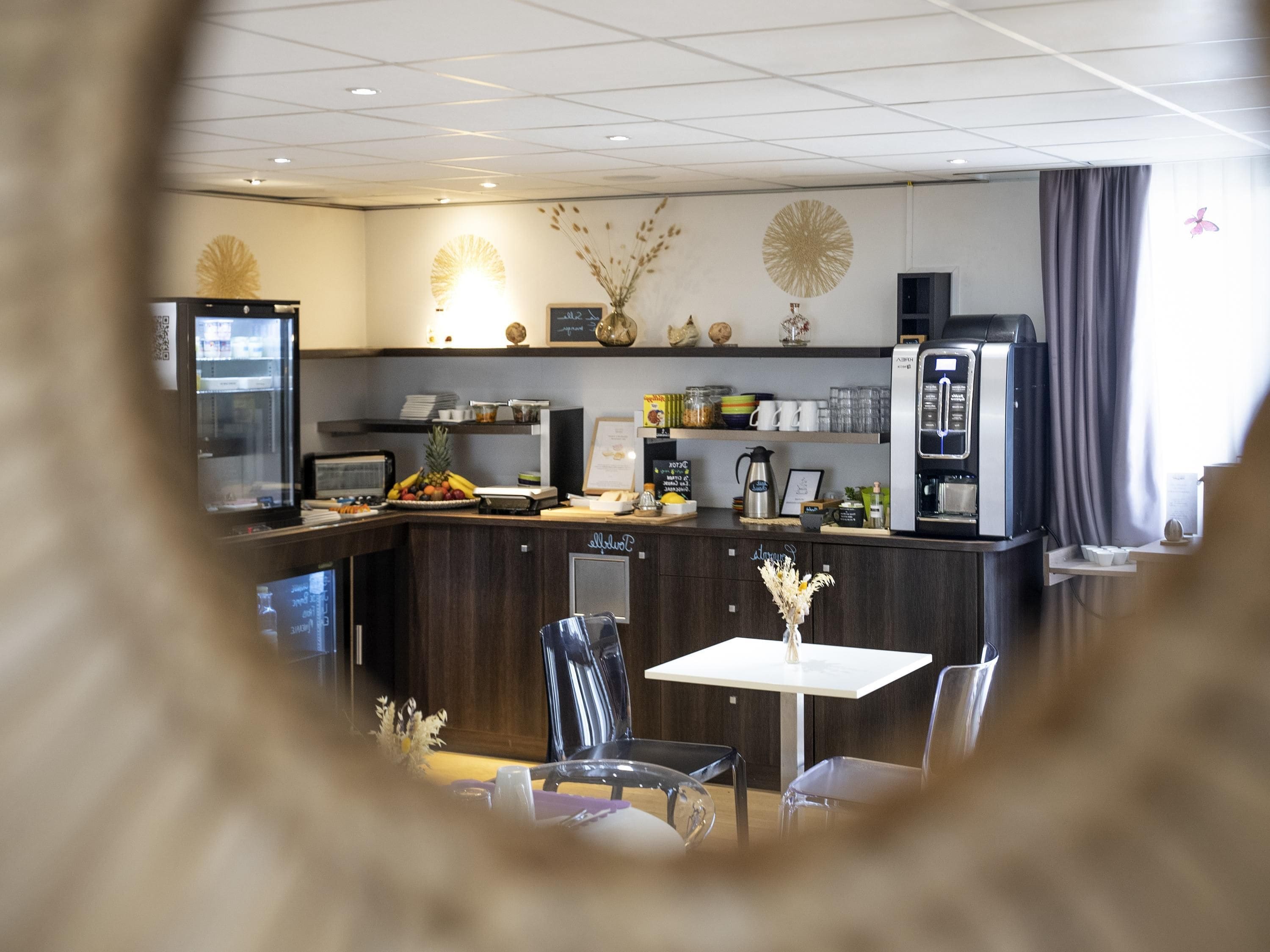 A modern kitchen area with a coffee machine, a refrigerator, and a dining table with chairs.