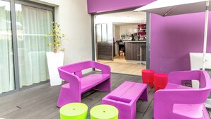A balcony with purple furniture, a potted plant, and a view into the kitchen area. - ibis Styles Rennes Saint Gregoire (Saint-Gregoire)