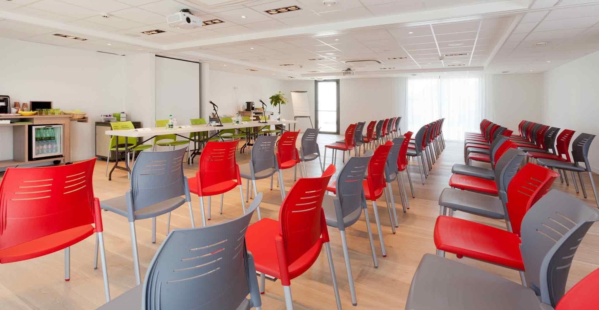Een vergaderruimte met rijen stoelen, een beamer, een whiteboard en een tafel met een laptop.