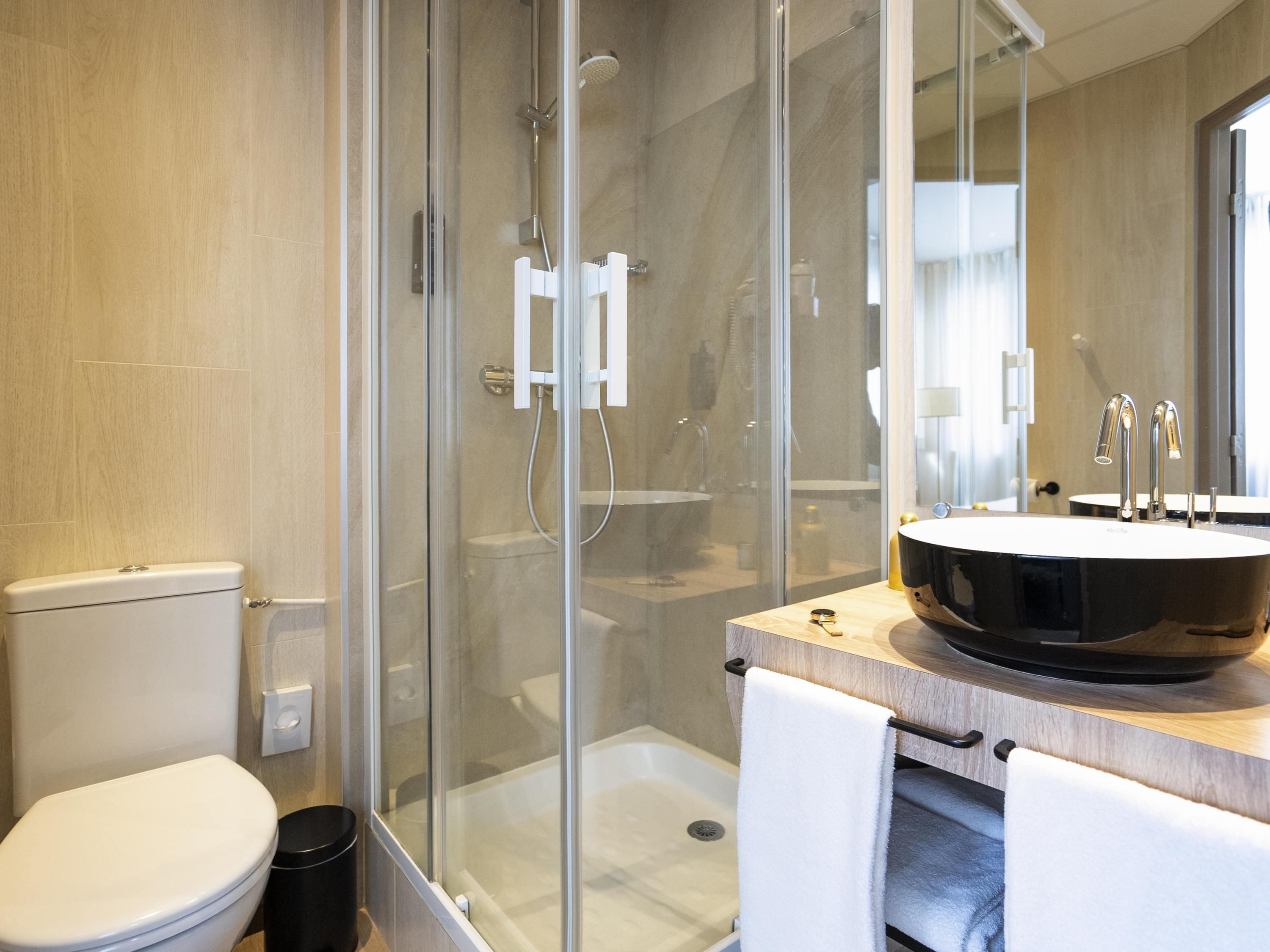 Een moderne badkamer met een douchecabine van glas, een toilet en een ruime wastafel met een rond wasbakje.