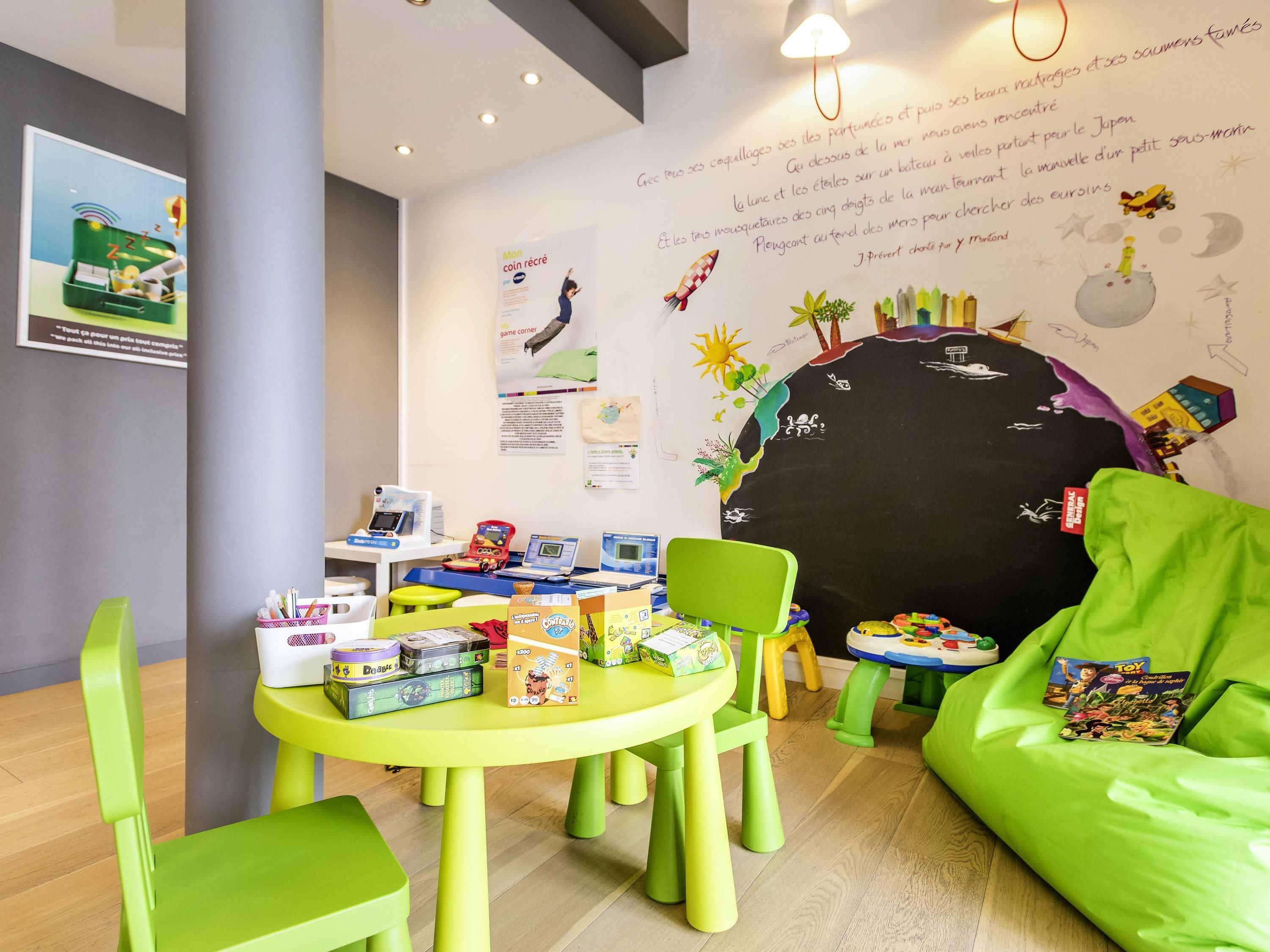 A children's play area with a round table, green chairs, and various toys.