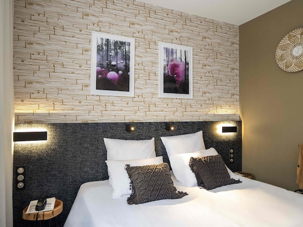 Ein Hotelzimmer mit einem Wandmuster, einem Bett mit weißen und gemusterten Kissen und zwei Bildern im Rahmen darüber.