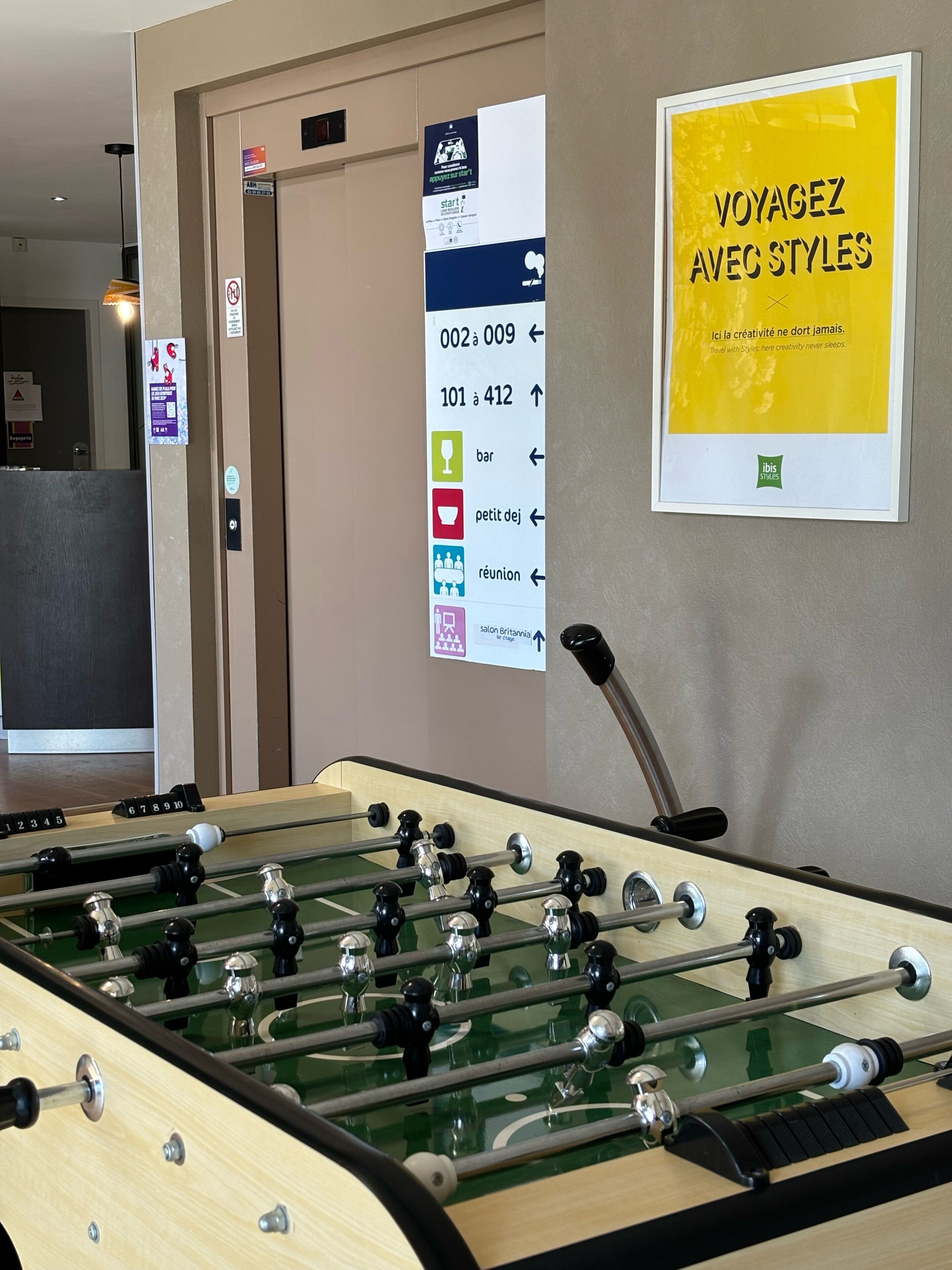 Una mesa de fútbol de mesa, un área de recepción con un cartel y un póster amarillo en la pared.