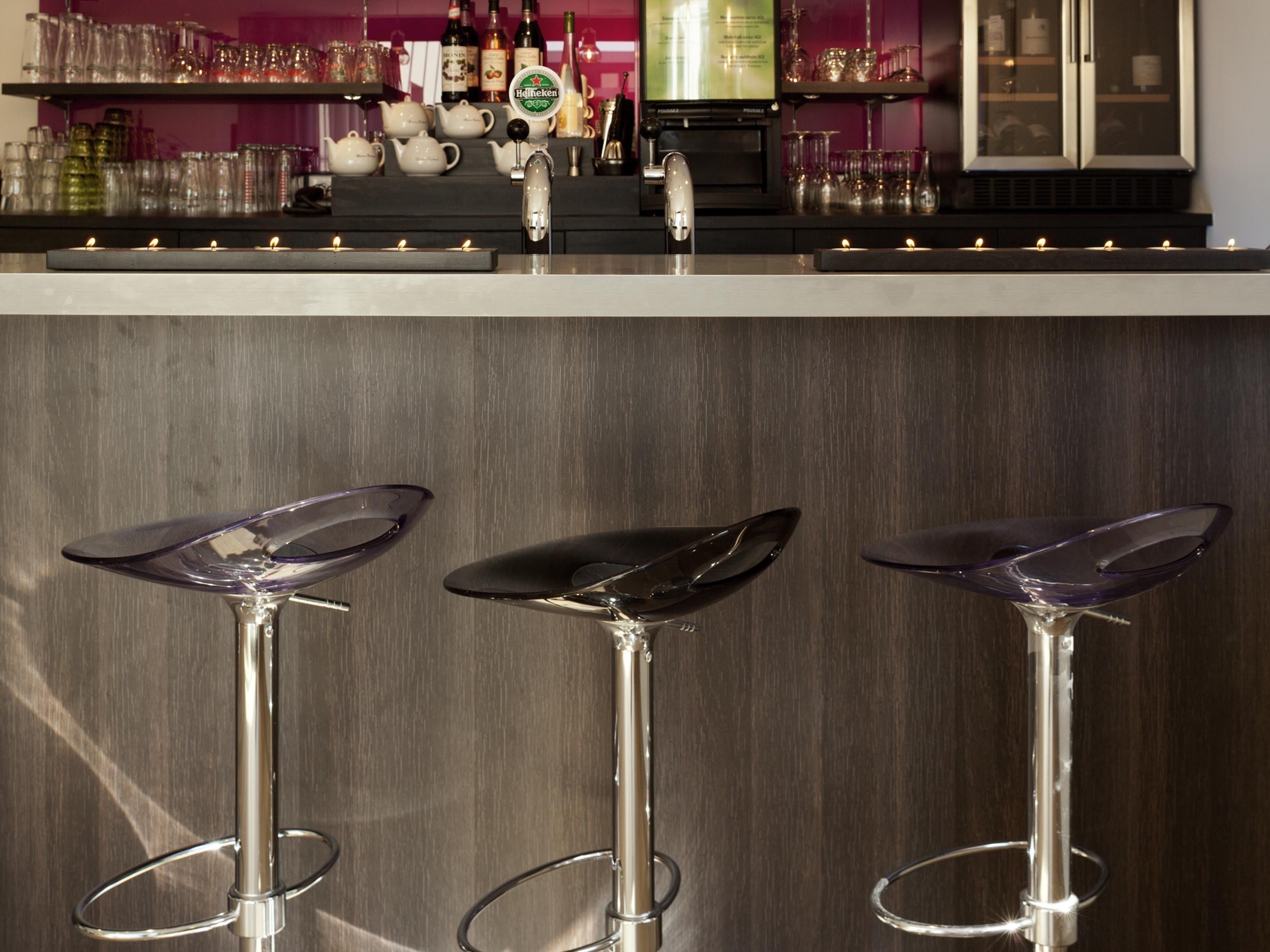 A bar area with three stools, a tap, and a display of bottles and glasses.