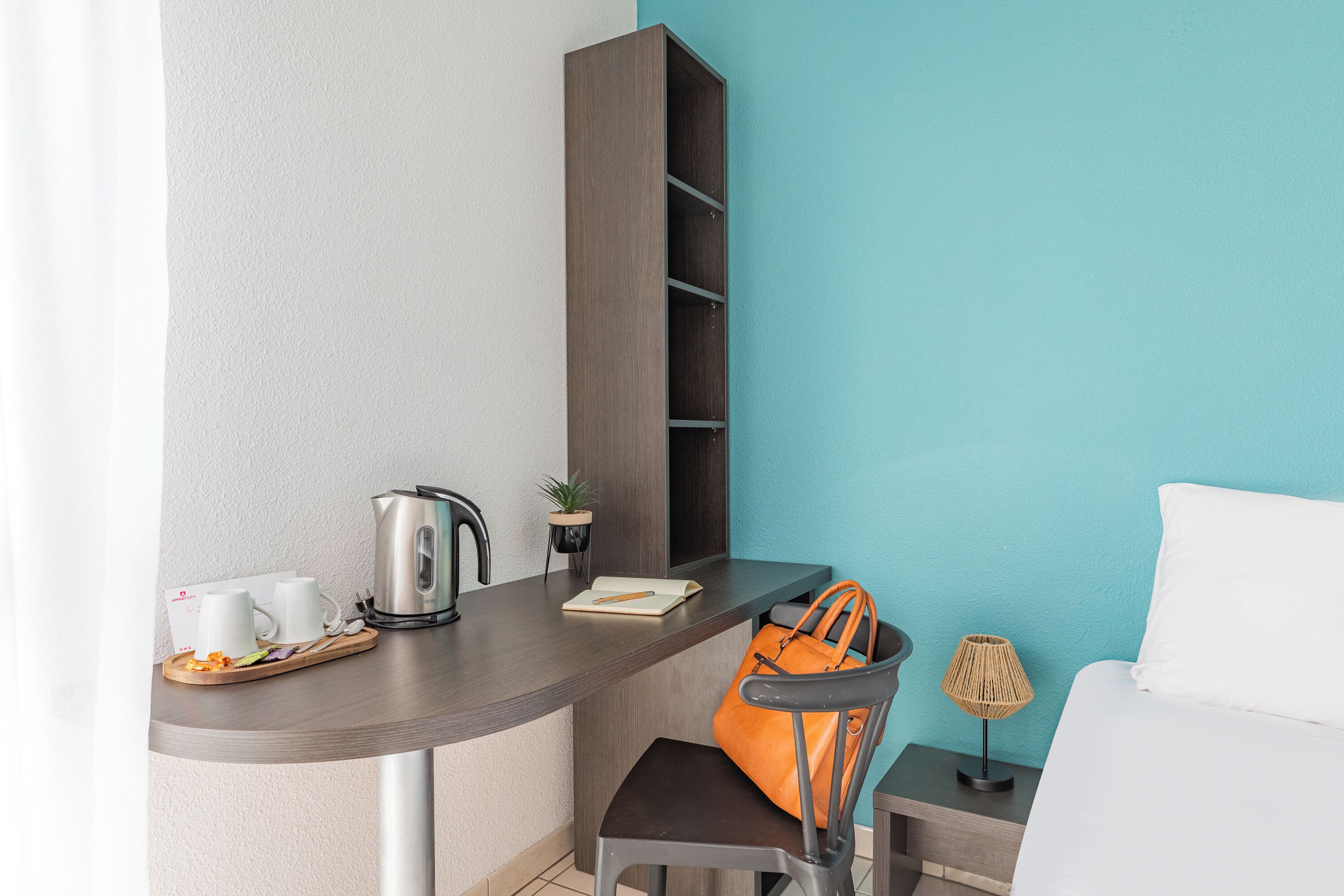 A compact room with a kitchenette, a small table, a chair, a sofa, and a lamp.