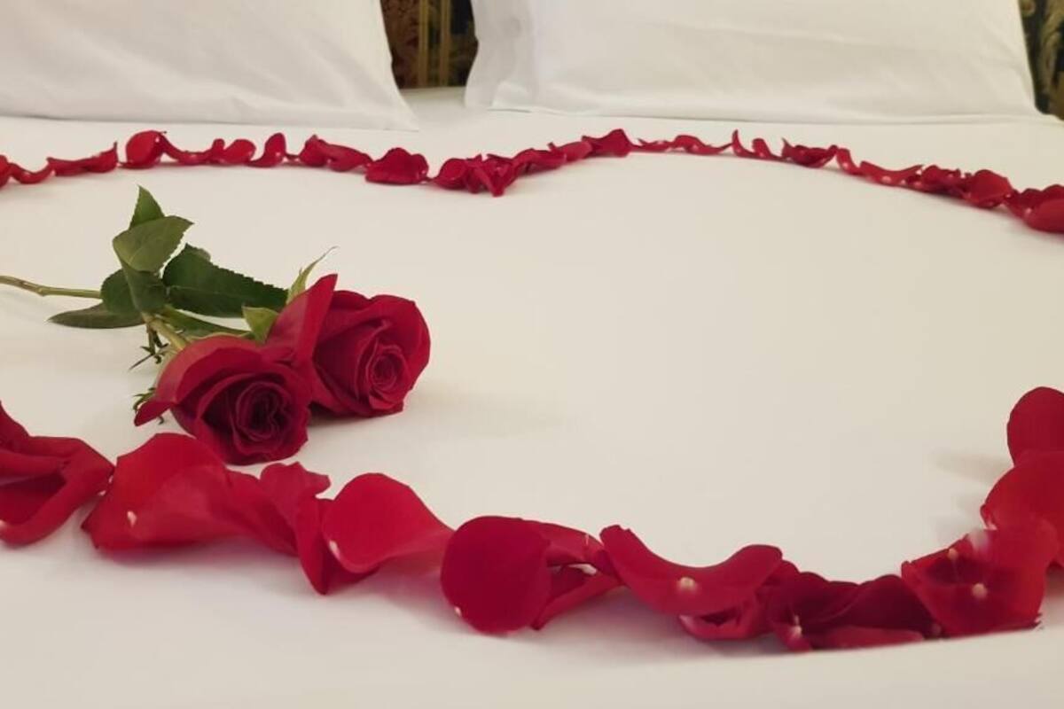 Un lit décoré de pétales de roses disposés en forme de cœur, avec une seule rose au centre.