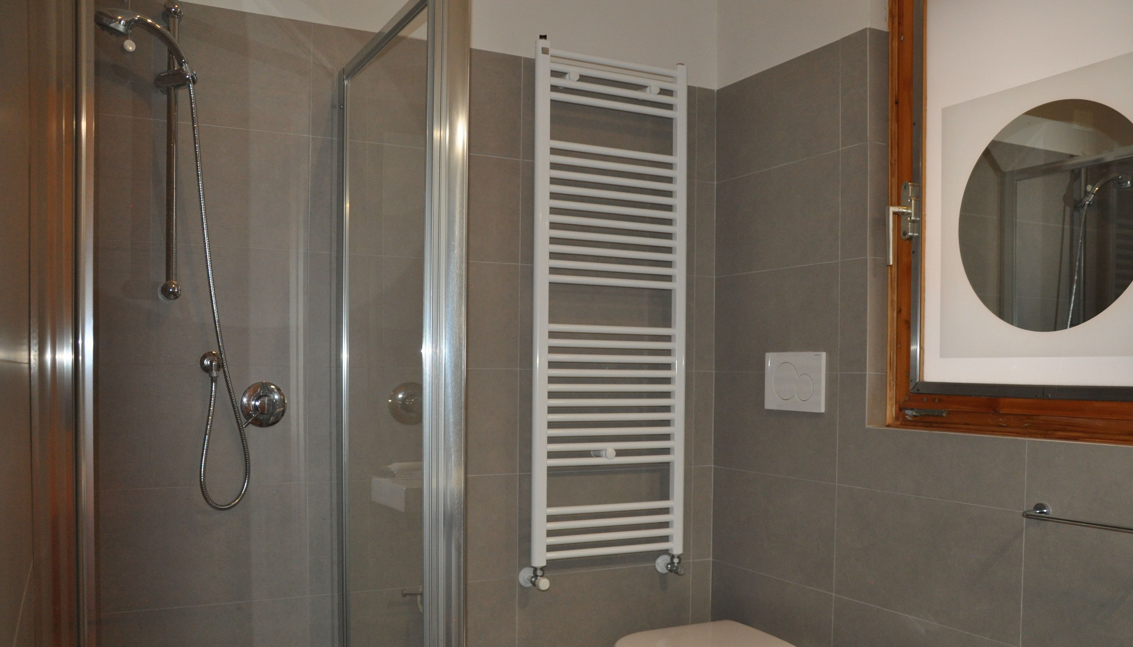 A bathroom with a glass shower enclosure, a white towel rack, and a mirror with a wooden frame.