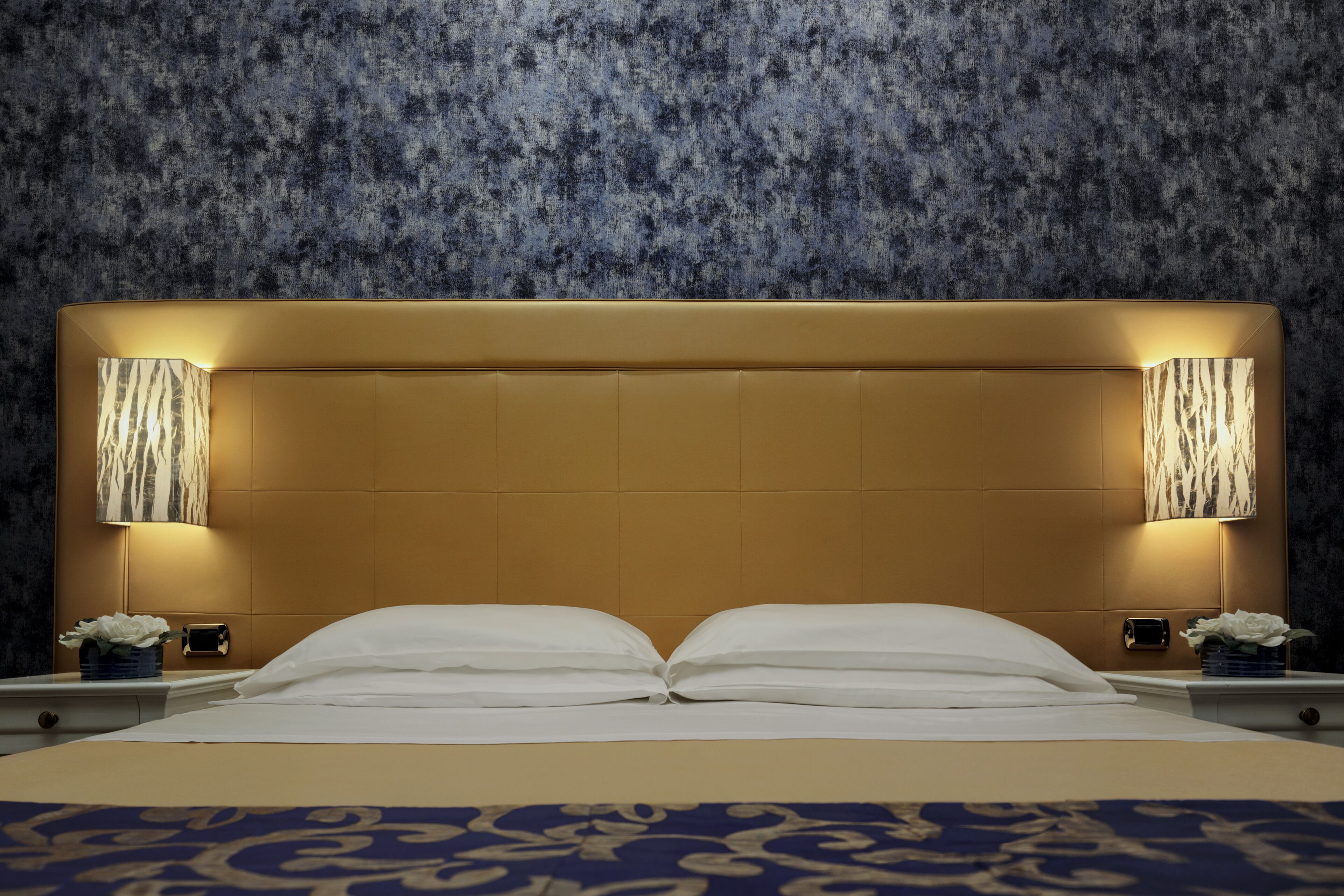 Habitación de hotel con una cama grande, dos lámparas de noche y una pared con textura.