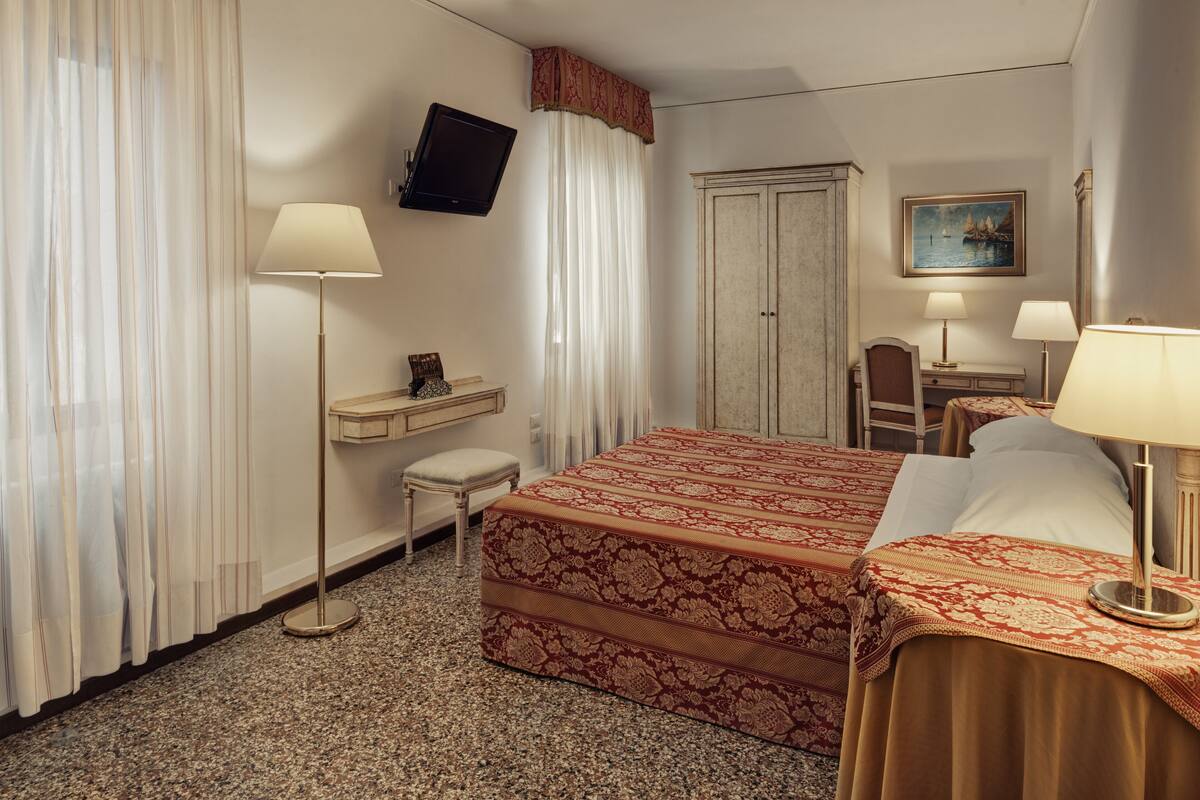 Une chambre d’hôtel comprenant un lit, deux tables de chevet, un bureau, une chaise, un téléviseur et une armoire.