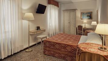 Habitación de hotel con cama, dos mesitas de noche, escritorio, silla, televisor y armario.