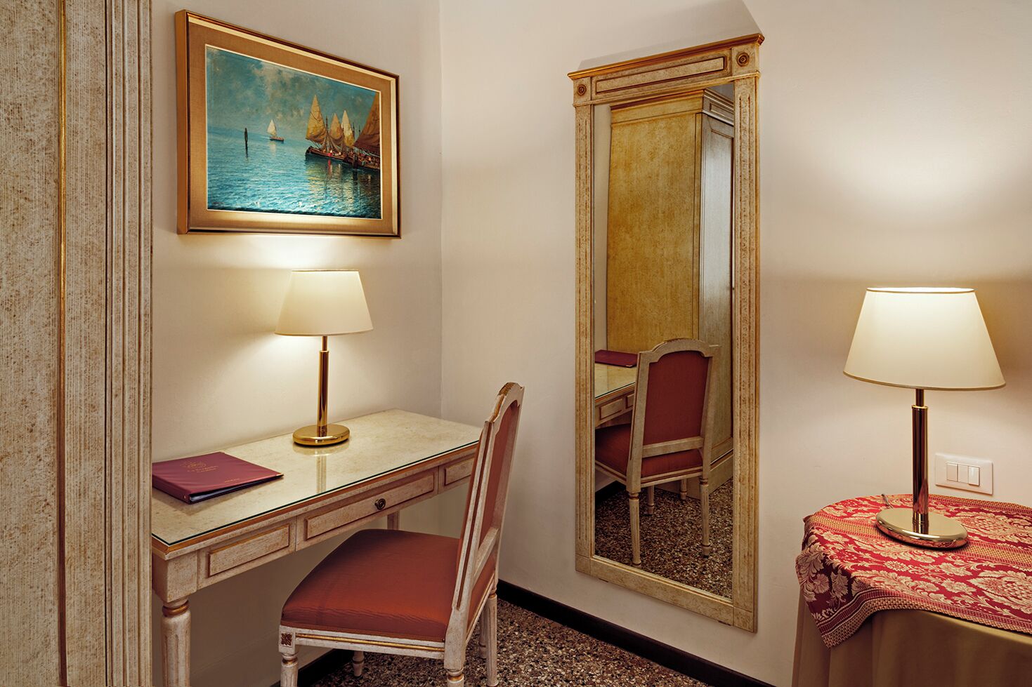 Habitació d'hotel amb escriptori, cadira, dues làmpades, un quadre i un mirall.