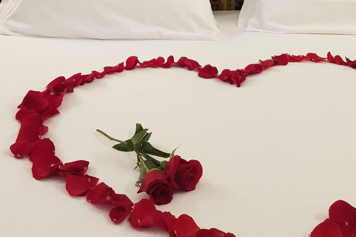 Un lit recouvert de draps blancs, agrémenté d’une composition en forme de cœur faite de pétales et de roses rouges.