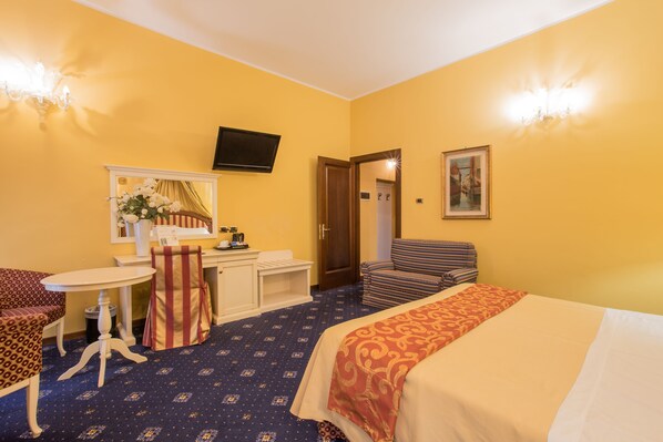 A hotel room with a bed, a desk, a chair, a television, and a door leading to another room.