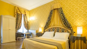 A hotel room with a large bed, a sitting area with a table and chairs, a wardrobe, and a patterned carpet. - Ca' Bragadin Carabba (Venice)