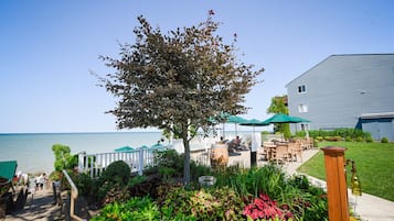 A coastal outdoor seating area with tables and chairs, a wooden fence, and a large tree.