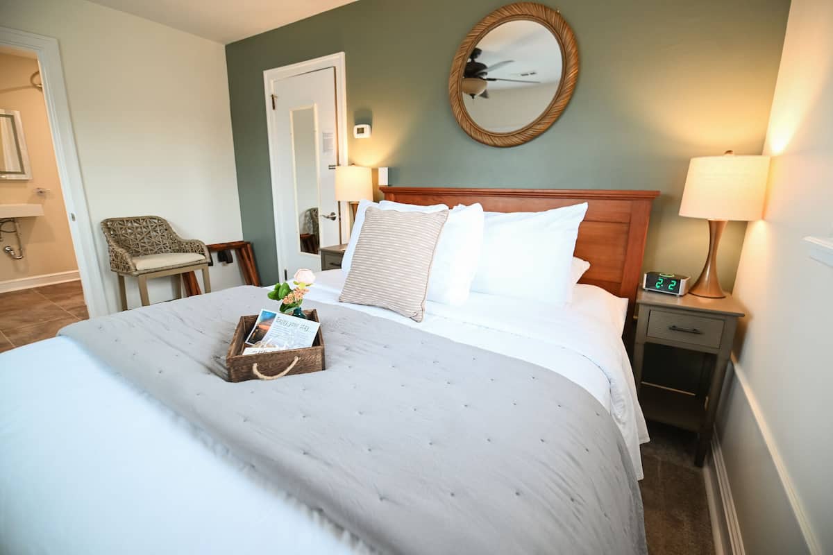 A neatly made bed with a wooden headboard, a bedside table with a lamp, and a small nightstand with a digital clock.