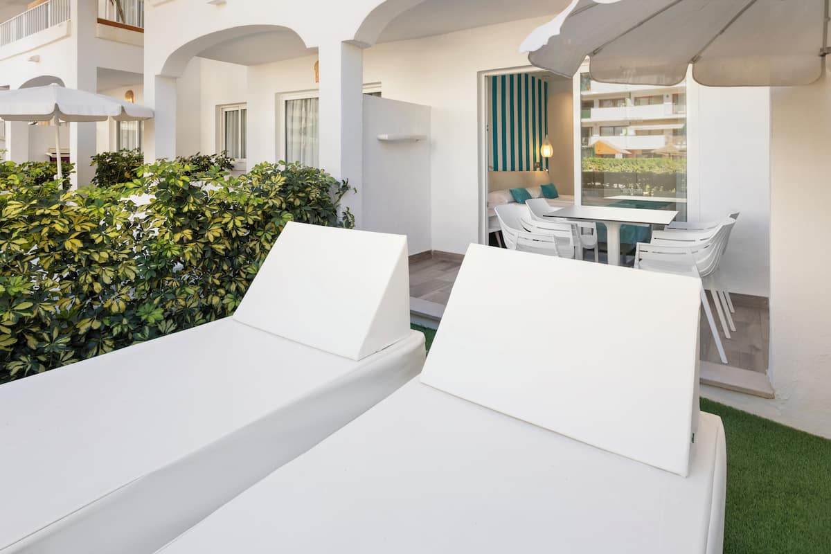 Een moderne terrasruimte met witte loungestoelen, een eettafel en een gebouw op de achtergrond.