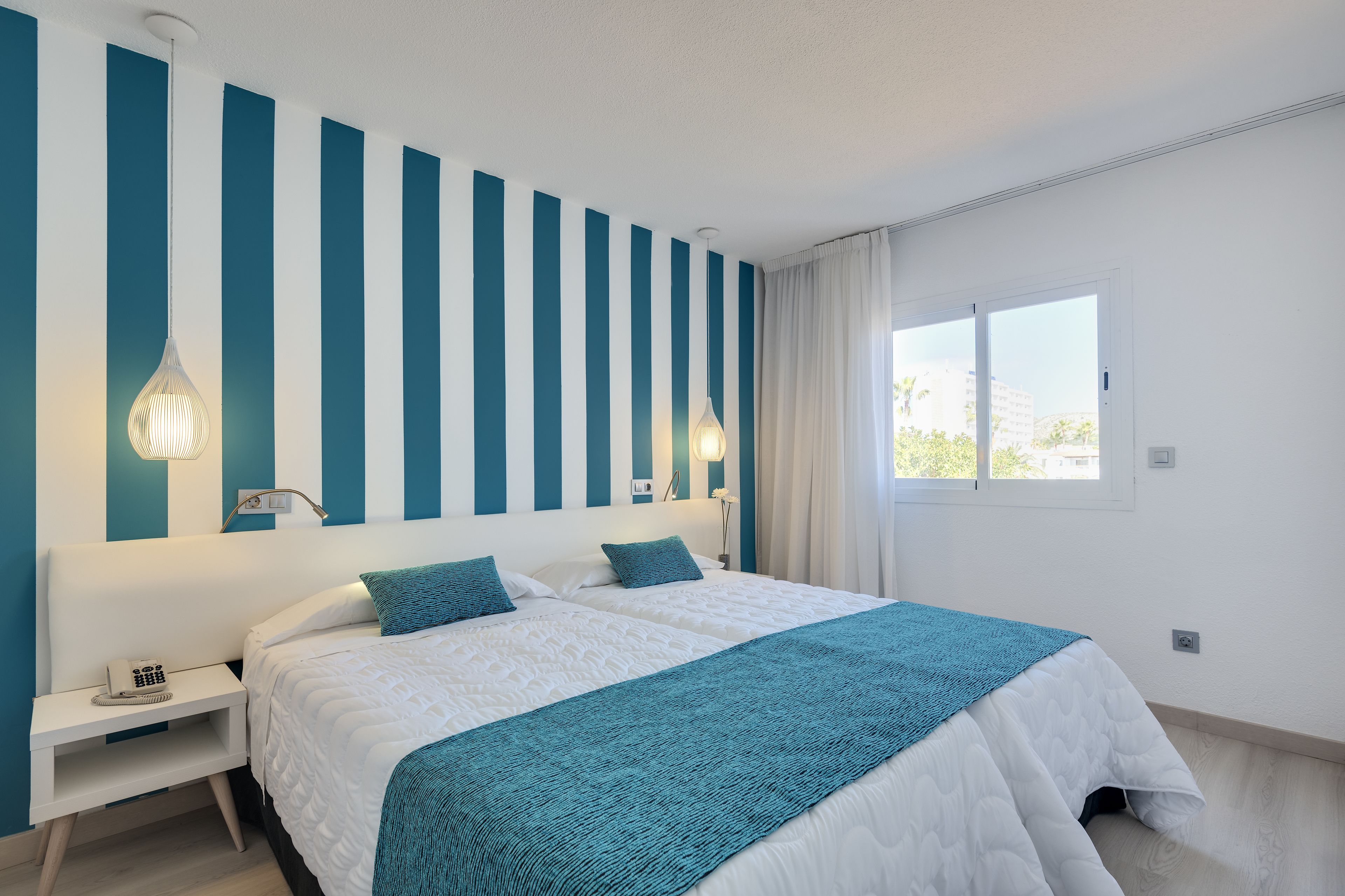 Un dormitorio con una cama grande, dos mesitas de noche y un ventanal con cortinas.