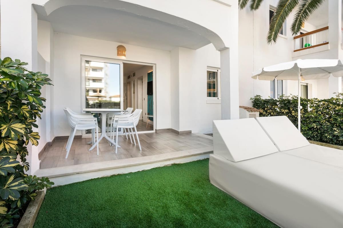 Een moderne buitenruimte met een witte bank, een eettafel met stoelen en een kleine tuin met kunstgras.