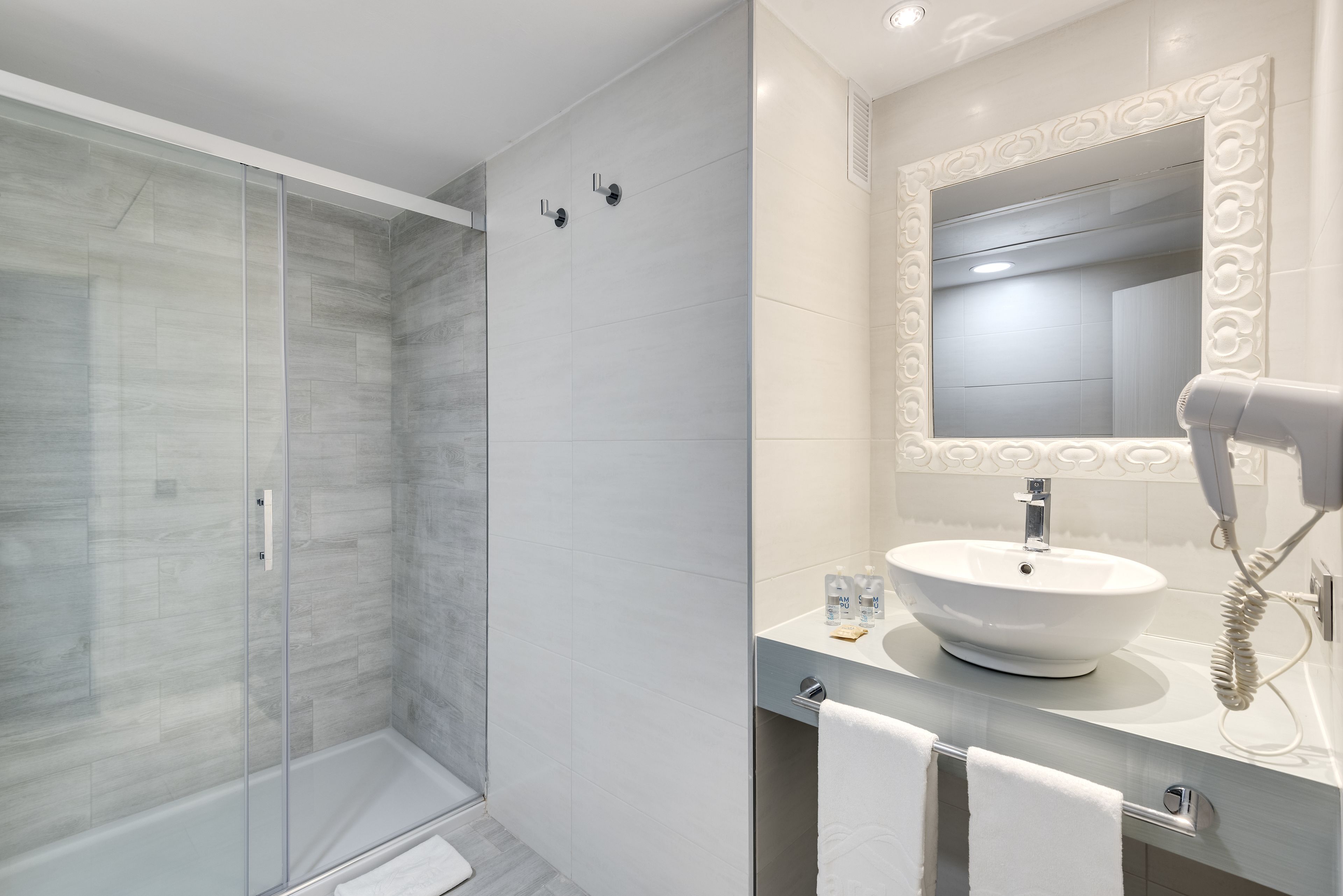 A modern bathroom with a glass shower enclosure, a white sink with a round basin, and a large mirror with an ornate frame.