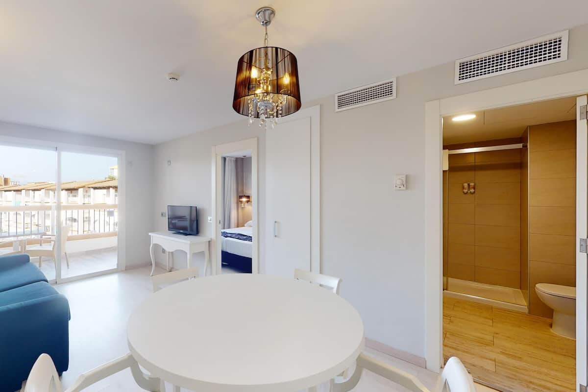 Een moderne hotelkamer met balkon, een ronde eettafel, een bank en een televisie.