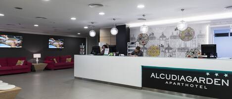 Un espace d’accueil au design moderne, comprenant un comptoir de réception, deux canapés rouges et une fresque murale décorative.