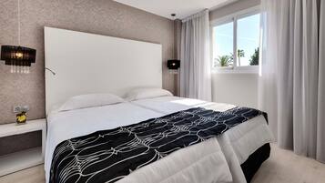 Una cama bien hecha con una colcha estampada, una mesita de noche con lámpara y una ventana con cortinas.