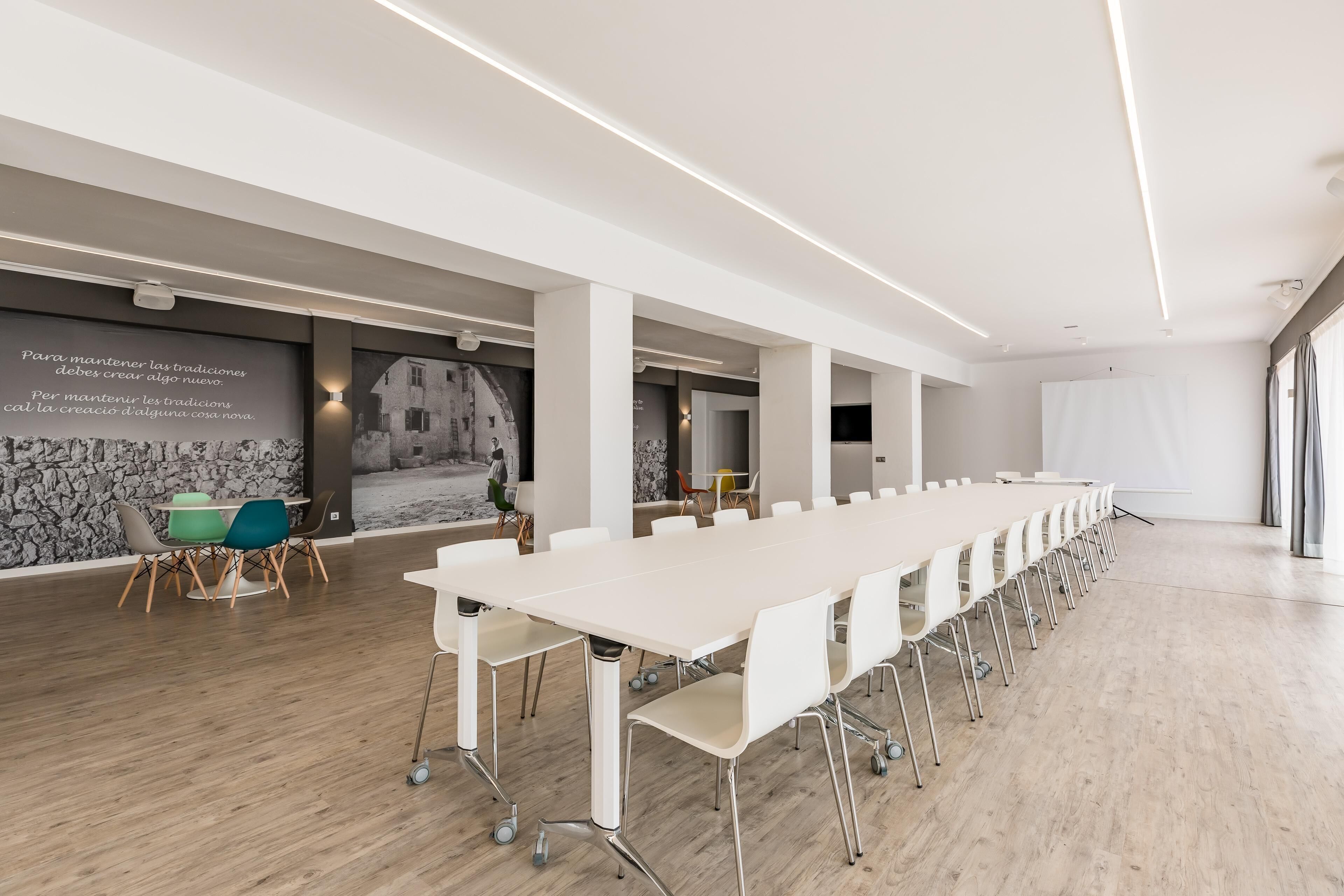 A modern conference room with a long white table, white chairs, and a stone wall with a black and white photo.