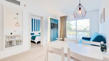 Habitación de hotel moderna con zona de comedor, televisor montado en la pared y balcón con vistas.