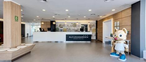 A modern reception area with a wooden reception desk, a mascot figure, and a wall with decorative artwork.