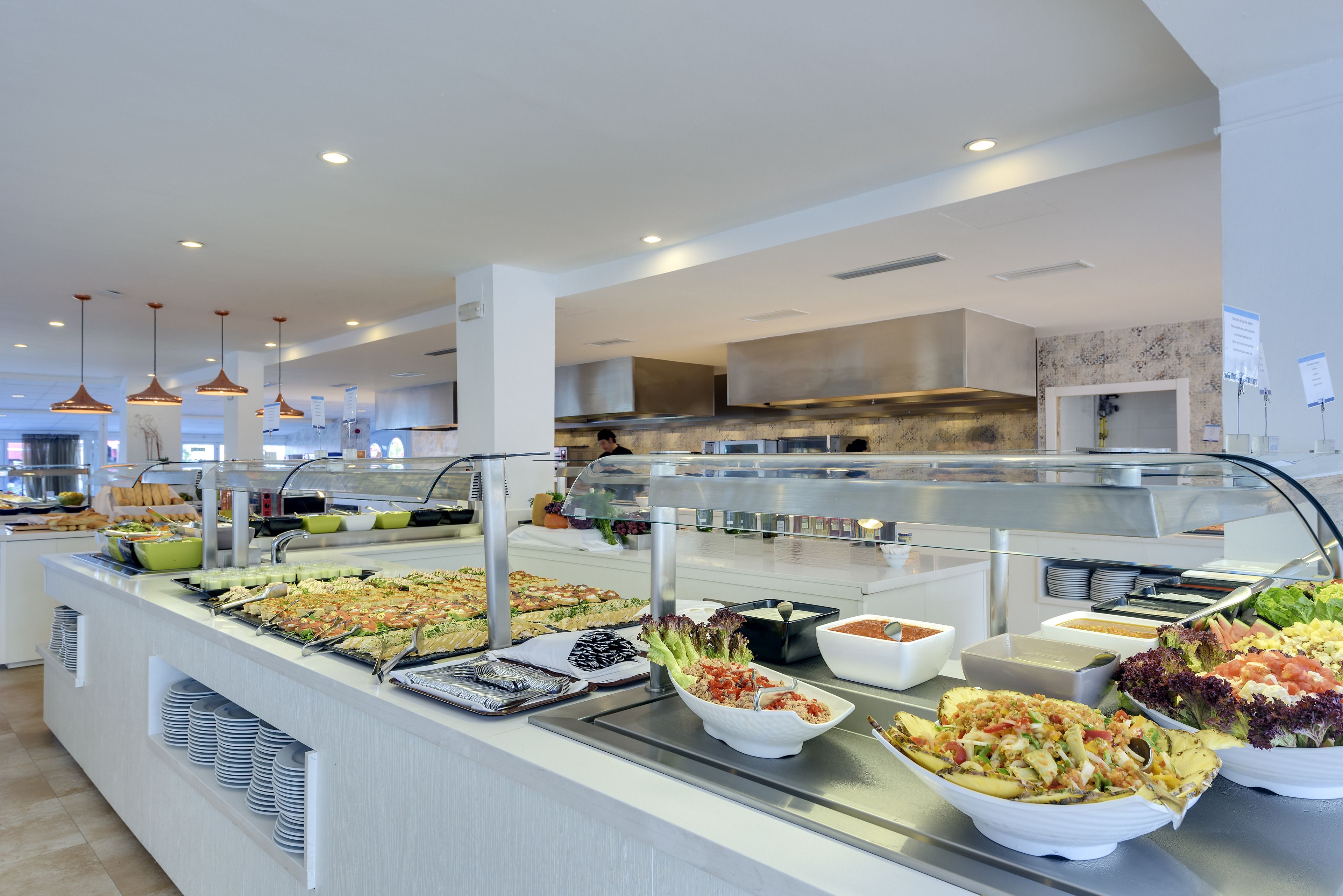 A buffet with various food options, a modern kitchen area in the background, and pendant lighting.