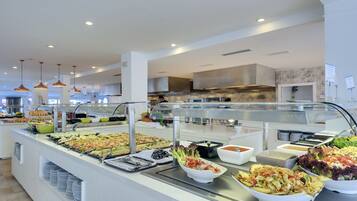 A buffet with various food options, a modern kitchen area in the background, and pendant lighting.