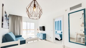 Una habitación de hotel moderna con una mesa de comedor blanca, un sofá azul y un espejo grande con marco azul.