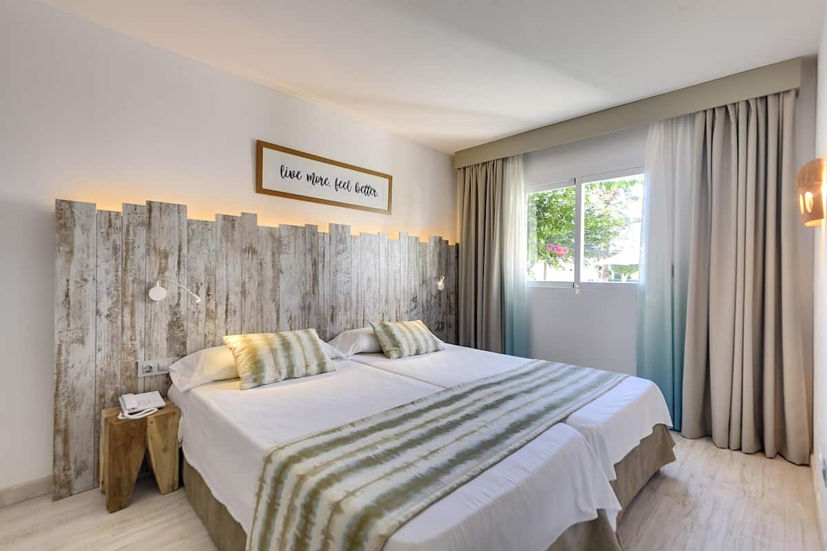 Een tweepersoonsbed met een gestreept dekbed, een houten hoofdbord, een bedtafeltelefoon en een motiverende quote op de muur.