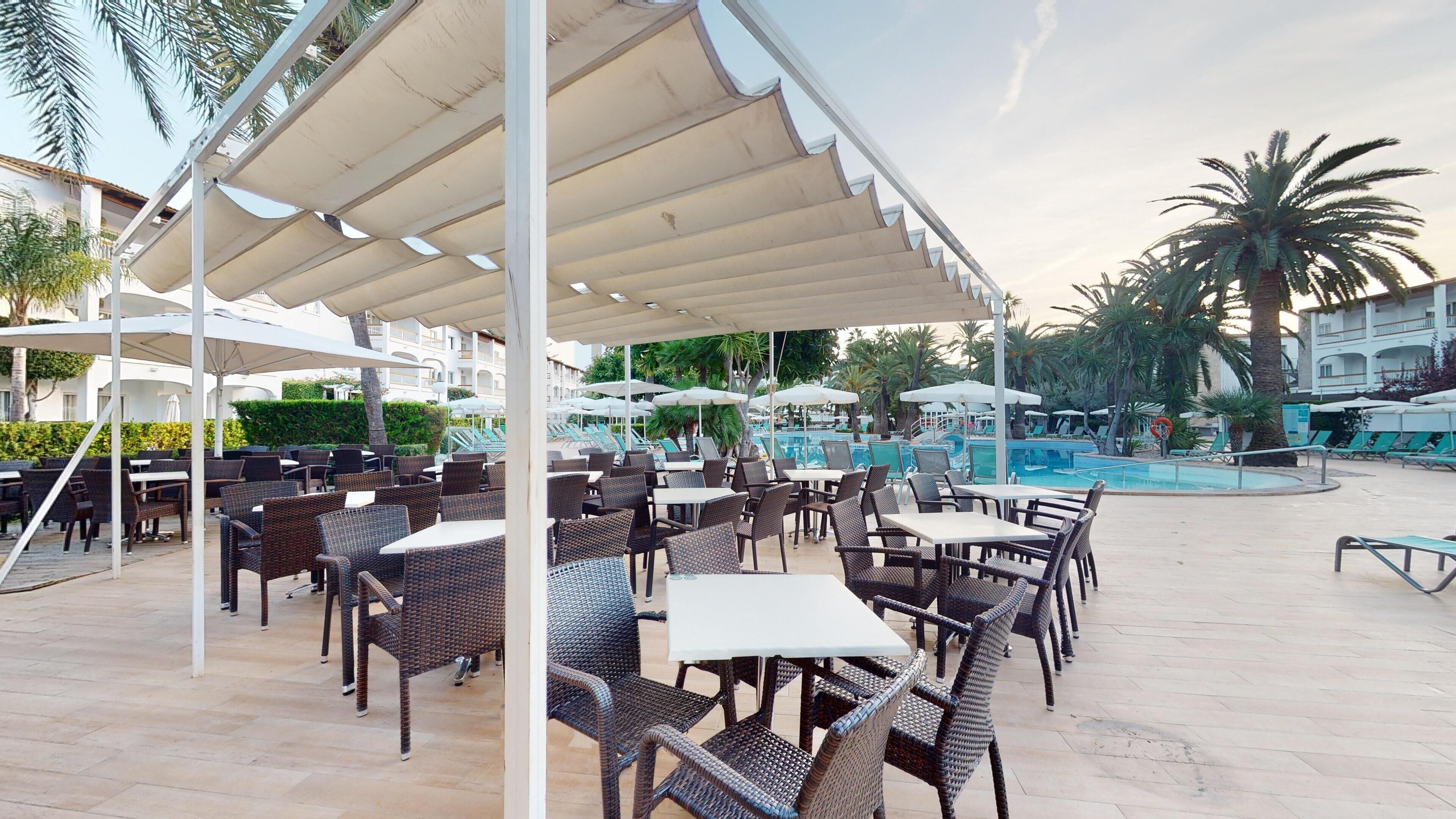 An outdoor seating area with wicker tables and chairs, a pool, and umbrellas.