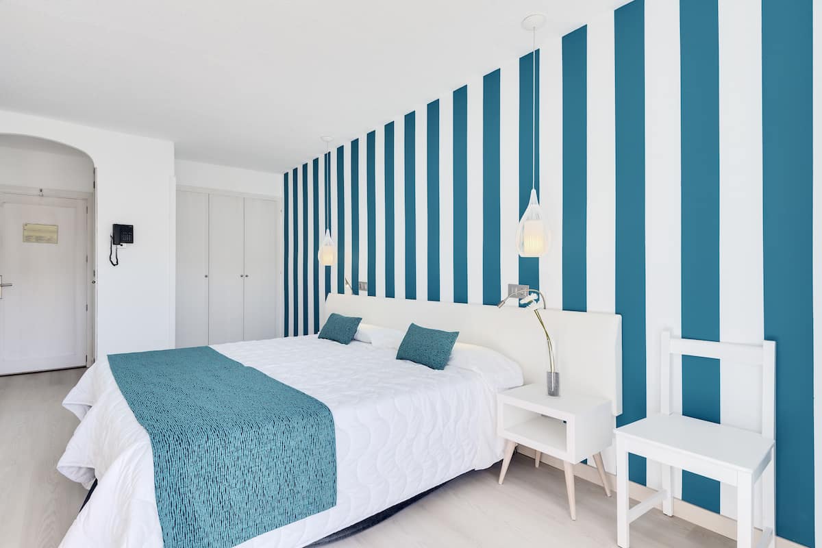 Een moderne hotelkamer met een groot bed, een wit hoofdbord en een blauw gestreepte wand.