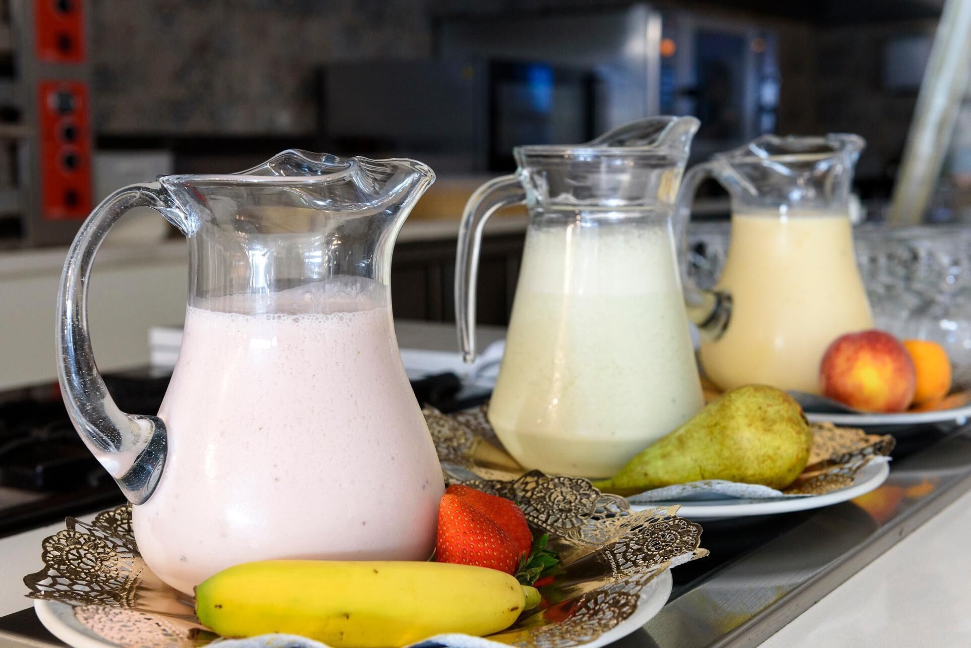 Three pitchers of a beverage, a banana, and a plate with fruits on a table.