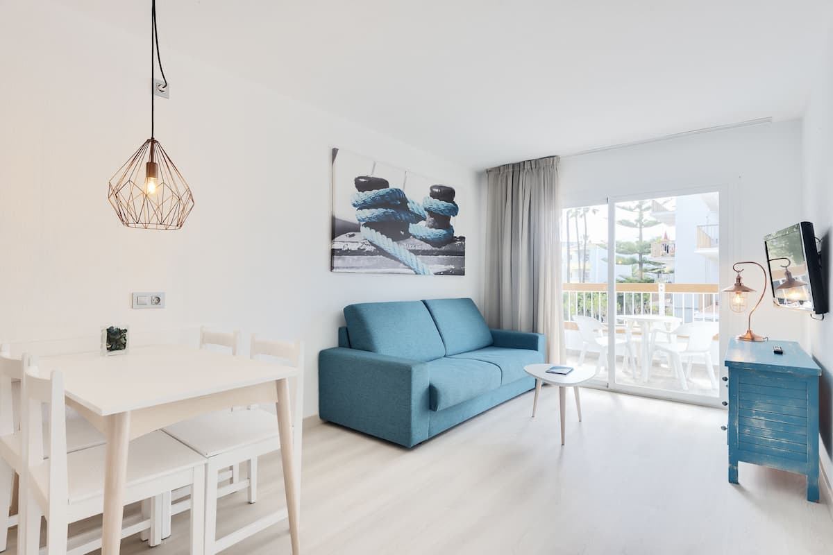 Een moderne woonkamer met een blauwe bank, een witte eettafel en een hanglamp.