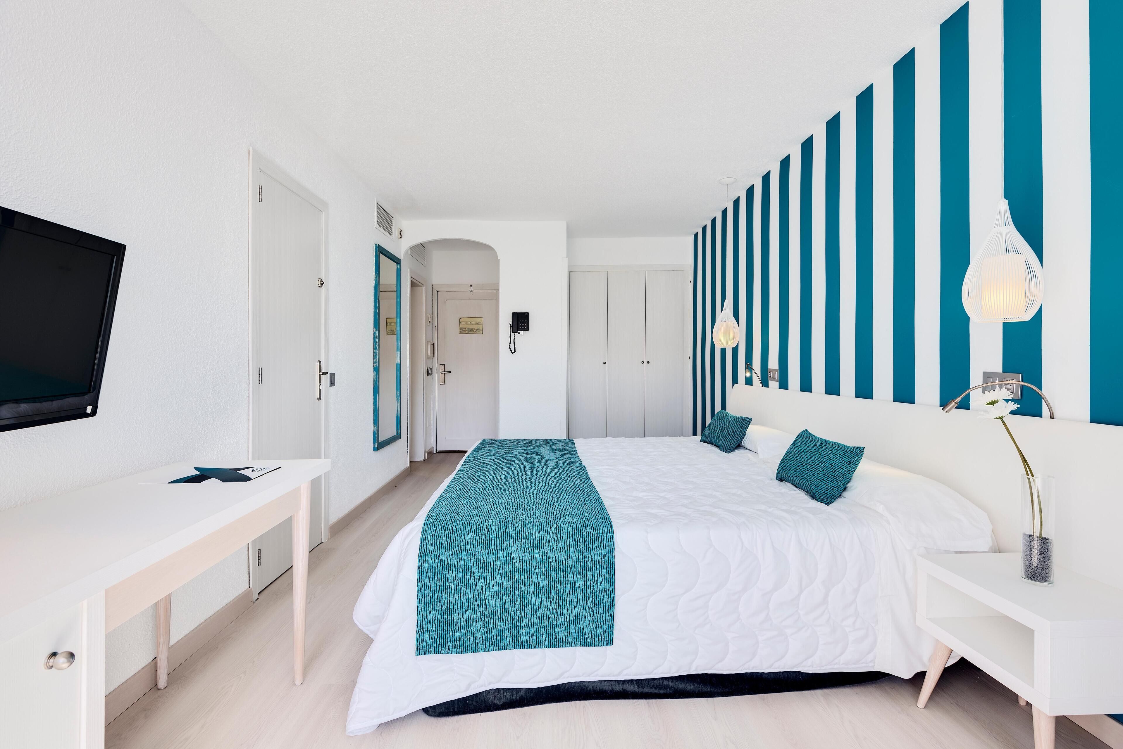 A modern hotel room with a large bed, a desk, a TV, and a striped wall.
