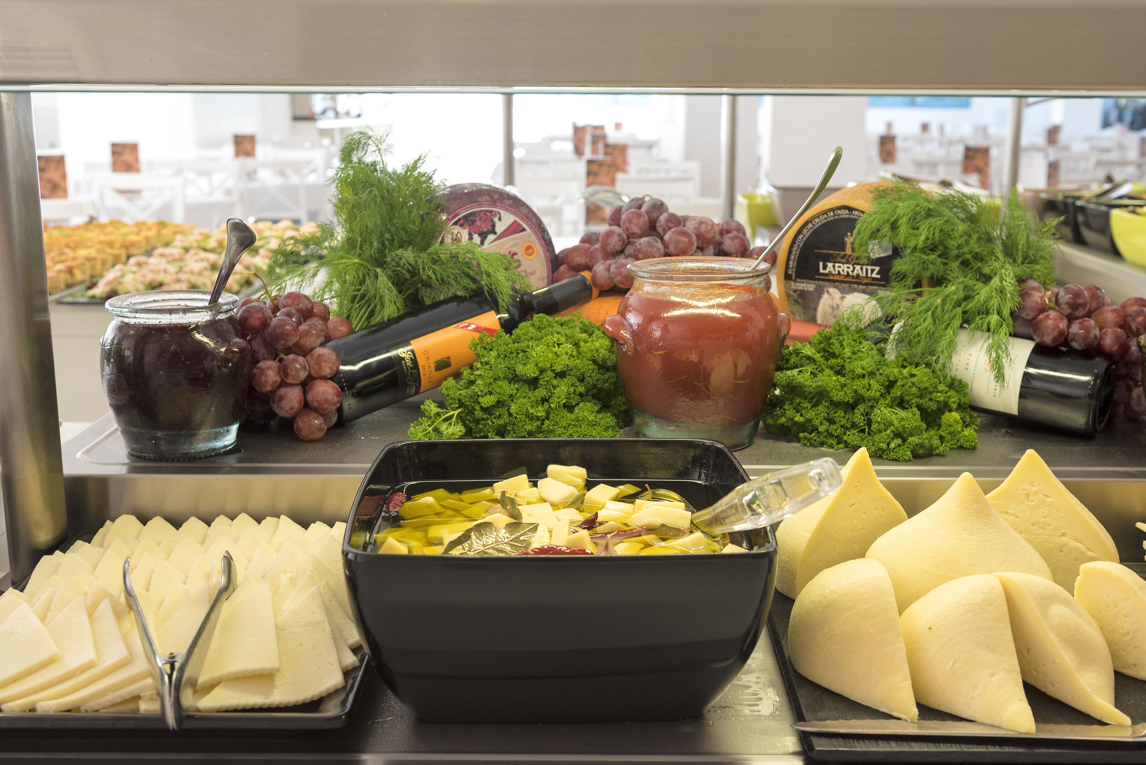 Un bufé con diversas opciones de comida, incluyendo queso, uvas y un frasco de salsa.