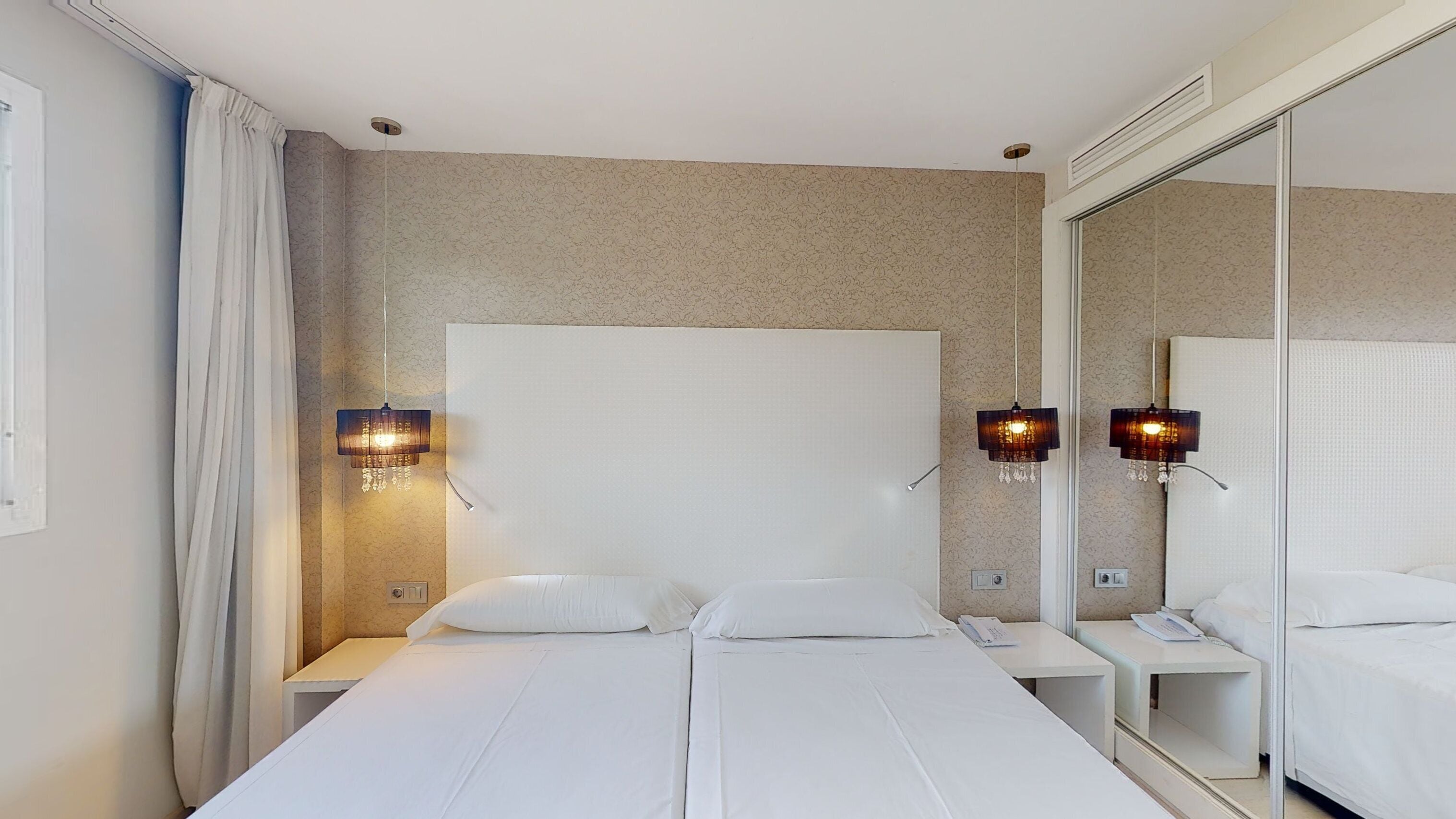 A hotel room with a large bed, two bedside tables, a mirror, and two wall-mounted lamps.