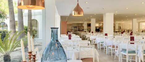 A spacious dining area with white tables and chairs, a large blue vase, and copper pendant lights.