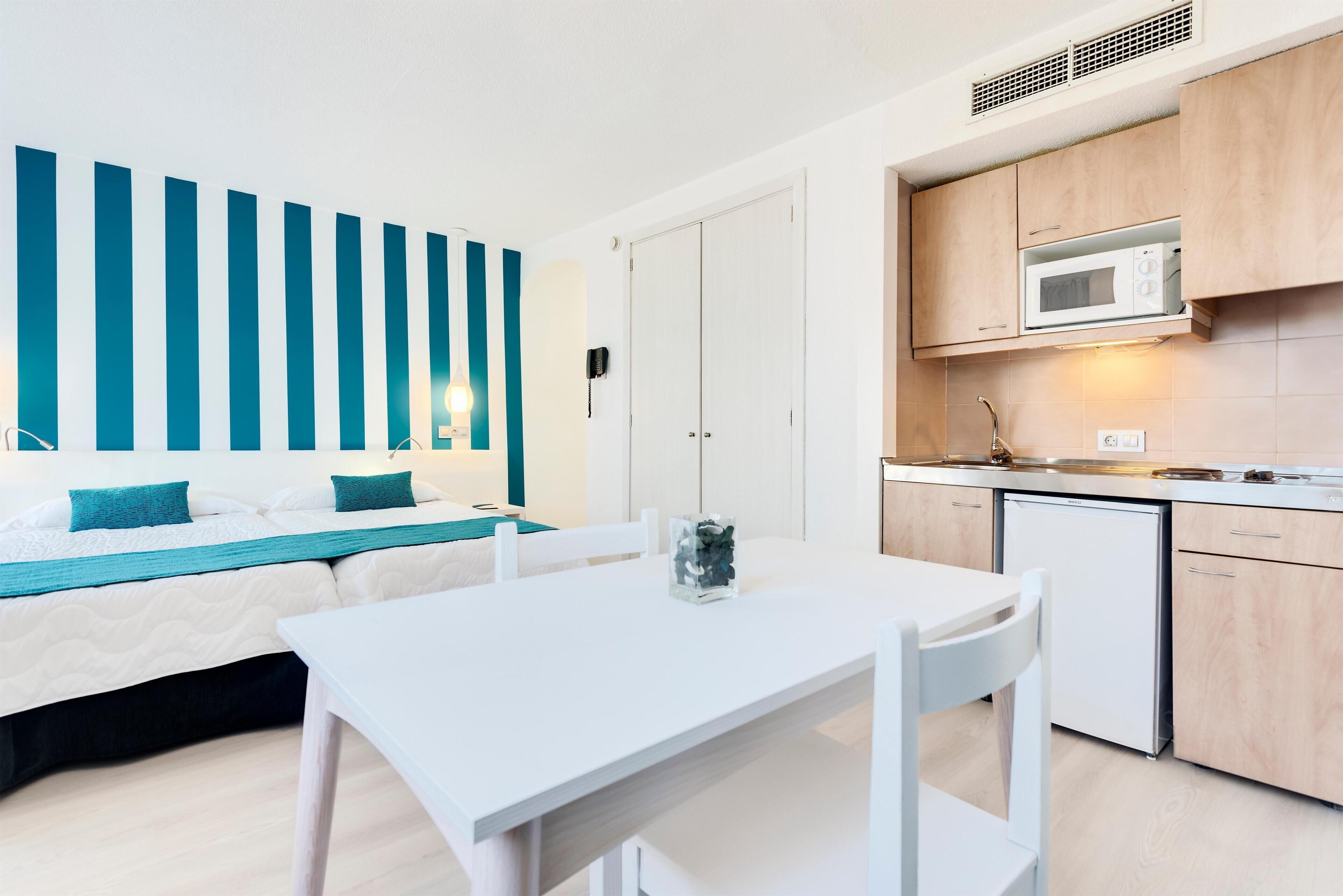 Una habitación de hotel moderna con una cama, una mesa blanca y una kitchenette.