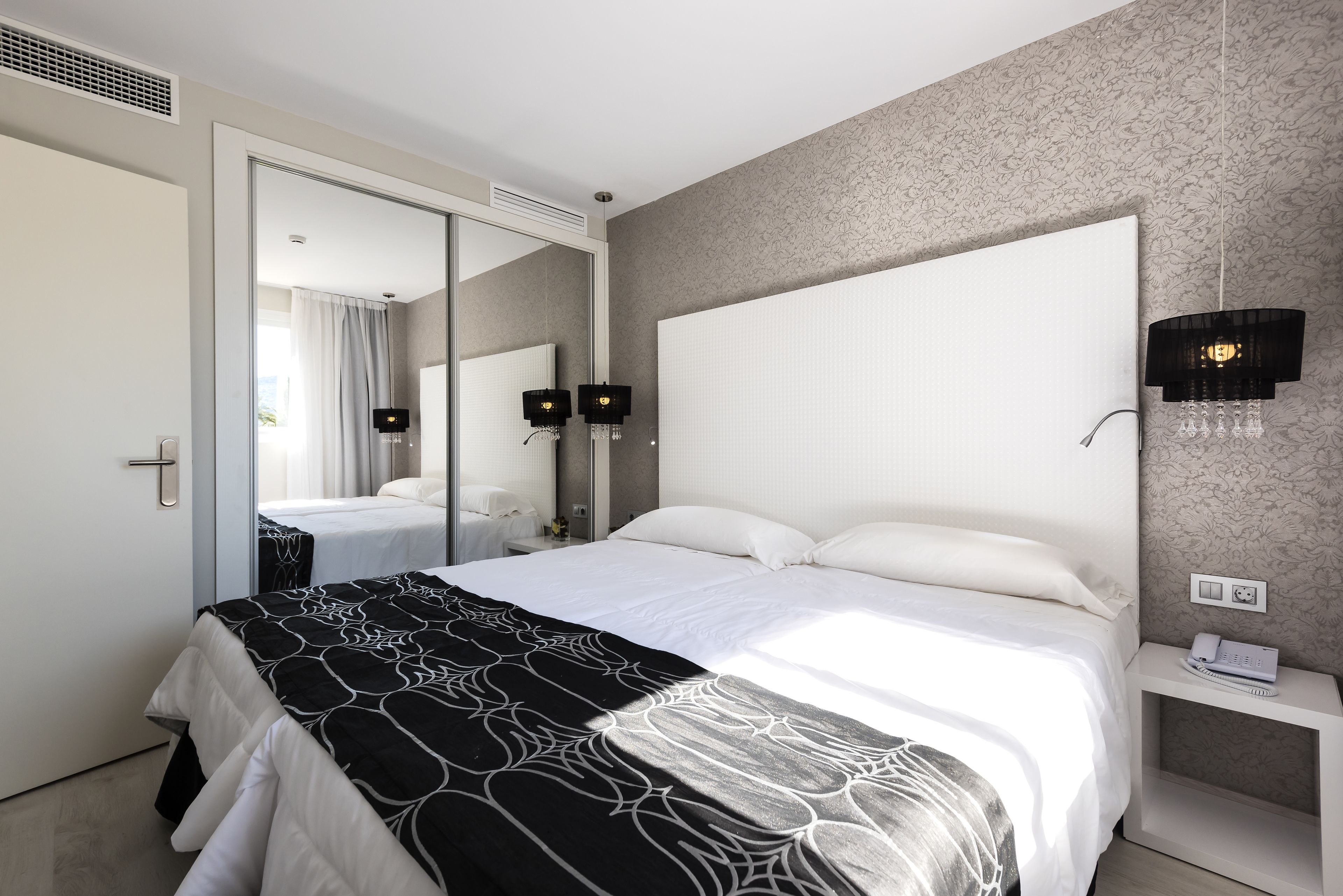 A modern hotel room with a large bed, a bedside table with a phone, and a mirror.