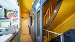 A hallway with a yellow wall, a door, and a staircase with a metal railing. - Princess Hostel Amsterdam (Amsterdam)