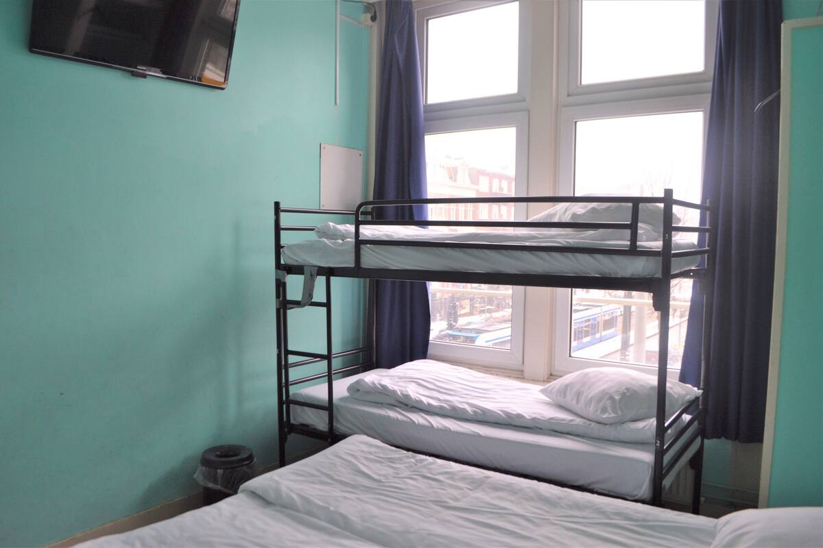 Une chambre avec un lit superposé, une fenêtre, un téléviseur fixé au mur et une vue sur l’extérieur.